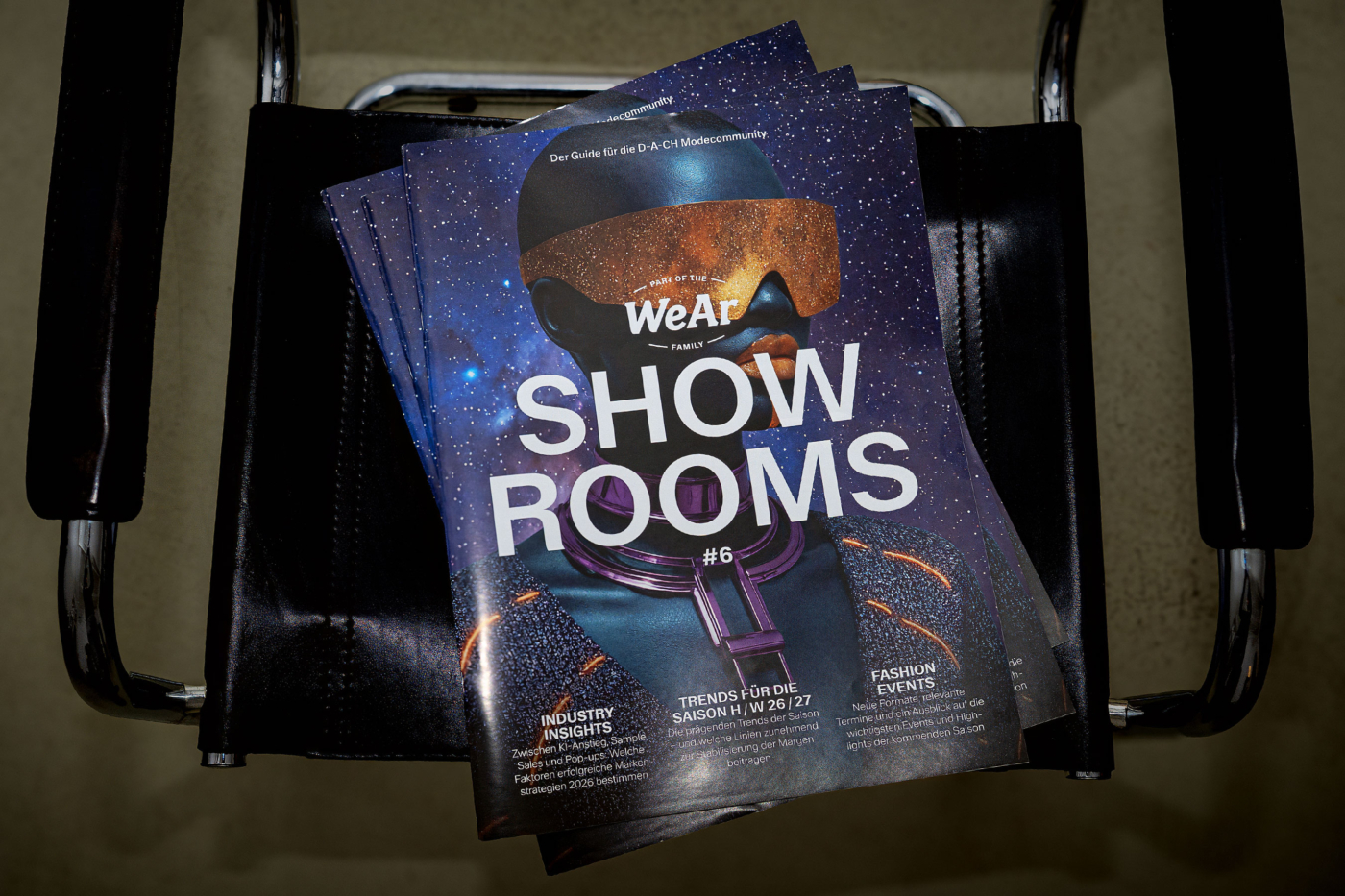 Mehrere Exemplare der sechsten Ausgabe der Fachzeitschrift 'WeAr Showrooms – Der Guide für die D-A-CH Modecommunity'. Die Titelseite zeigt ein futuristisches Design mit einem stilisierten Porträt und dem Titel 'SHOW ROOMS #6' sowie den Unterthemen 'Industry Insights', 'Trends für die Saison H/W 26/27' und 'Fashion Events.